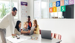 Primary school children and teacher working on robot programming - Coding kids sign in the background