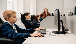Primary school children working on computers in class with teacher
