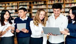 Secondary school pupils standing looking at laptop in library