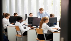 Secondary school pupils working on computers with teacher helping
